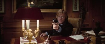 Movie still from “Three Days of the Condor” (1975), directed by Sydney Pollack – A man sitting at a table holding a gun; Medium shot, Low angle