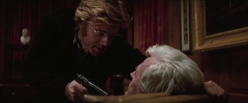 Movie still from “Three Days of the Condor” (1975), directed by Sydney Pollack – A man holding a gun near another man in a chair; Close Up shot, Over the shoulder angle