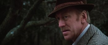 Movie still from “Three Days of the Condor” (1975), directed by Sydney Pollack – A person wearing a hat with trees in the background; Close Up shot, Over the shoulder angle