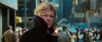 Movie still from “Three Days of the Condor” (1975), directed by Sydney Pollack – A man with blonde hair and glasses is wearing a black coat; Close Up shot, Low angle