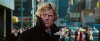 Movie still from “Three Days of the Condor” (1975), directed by Sydney Pollack – A man with blonde hair wearing glasses and a black coat; Close Up shot, Low angle