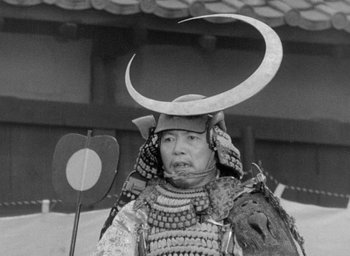 Movie still from “Throne of Blood” (1957), directed by Akira Kurosawa – An older man wearing a horned hat in a black - and - white photo; Close Up shot, Low angle