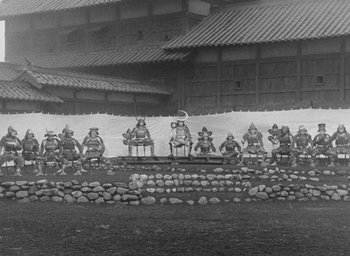 Movie still from “Throne of Blood” (1957), directed by Akira Kurosawa – A group of men in traditional garb sitting on rocks; Extreme Wide shot, High angle
