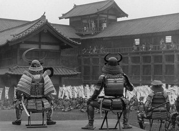 Movie still from “Throne of Blood” (1957), directed by Akira Kurosawa – A group of men sitting on chairs in front of a building; Extreme Wide shot, High angle