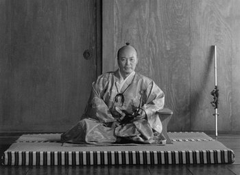 Movie still from “Throne of Blood” (1957), directed by Akira Kurosawa – An asian man sitting on top of a piano keyboard; Medium shot, Low angle