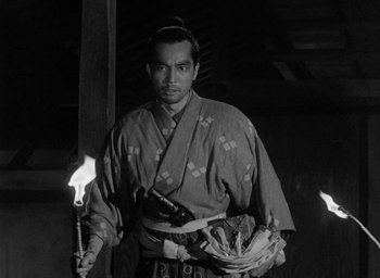 Movie still from “Throne of Blood” (1957), directed by Akira Kurosawa – A man in traditional japanese garb holding torches; Medium shot, Low angle