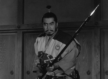 Movie still from “Throne of Blood” (1957), directed by Akira Kurosawa – A man holding a sword while wearing an oriental outfit; Medium shot, Low angle