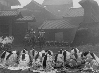 Movie still from “Throne of Blood” (1957), directed by Akira Kurosawa – A black and white photo of people sitting on the ground; Extreme Wide shot, High angle
