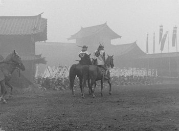 Movie still from “Throne of Blood” (1957), directed by Akira Kurosawa – Two men on horses in a field with a crowd of onlookers in the background; Wide shot, Low angle