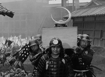 Movie still from “Throne of Blood” (1957), directed by Akira Kurosawa – A group of men in samurai garb standing next to each other; Wide shot, Over the shoulder angle