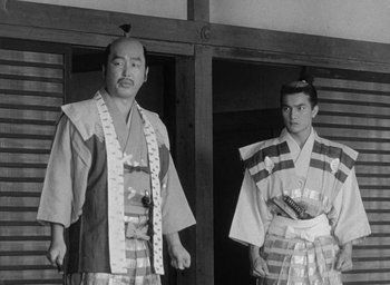 Movie still from “Throne of Blood” (1957), directed by Akira Kurosawa – Two men standing next to each other in traditional japanese clothing; Medium shot, Low angle