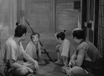Movie still from “Throne of Blood” (1957), directed by Akira Kurosawa – A black and white photo of a group of people sitting on the ground; Wide shot, Over the shoulder angle