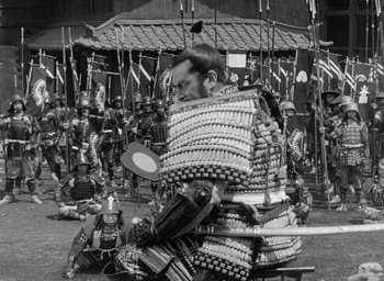 Movie still from “Throne of Blood” (1957), directed by Akira Kurosawa – A man in samurai garb holding a sword in front of a group of people; Wide shot, High angle
