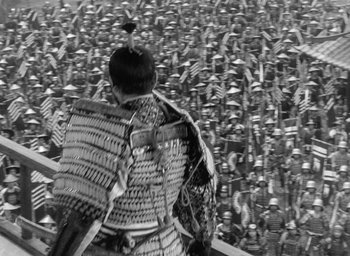 Movie still from “Throne of Blood” (1957), directed by Akira Kurosawa – A person in a crowd of people wearing a costume; Extreme Wide shot, High angle