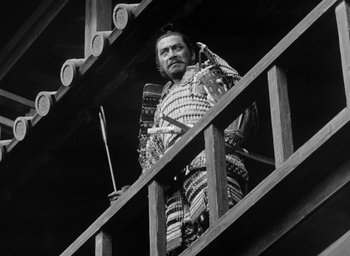 Movie still from “Throne of Blood” (1957), directed by Akira Kurosawa – A man in a suit of armor standing on a wooden platform; Medium shot, Low angle