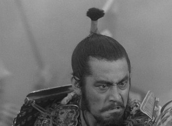 Movie still from “Throne of Blood” (1957), directed by Akira Kurosawa – A man with a beard and a mustache with a hair piece on top of his head; Close Up shot, Over the shoulder angle