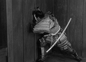 Movie still from “Throne of Blood” (1957), directed by Akira Kurosawa – A man in samurai garb is holding a sword; Medium shot, High angle