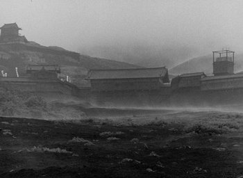 Movie still from “Throne of Blood” (1957), directed by Akira Kurosawa – A black - and - white photo of a foggy landscape with buildings; Extreme Wide shot, Low angle