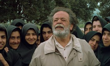 Movie still from “Through the Olive Trees” (1994), directed by Abbas Kiarostami – An old man with a beard and a group of people; Medium shot, Low angle