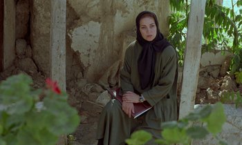 Movie still from “Through the Olive Trees” (1994), directed by Abbas Kiarostami – A woman sitting on the ground holding a laptop; Medium shot, High angle