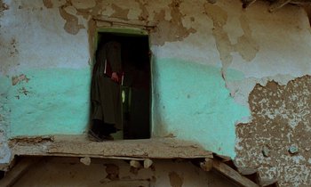 Movie still from “Through the Olive Trees” (1994), directed by Abbas Kiarostami – A person standing in an open doorway of an abandoned building; Wide shot, Low angle