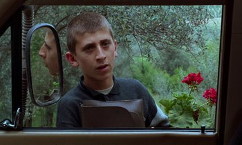 Movie still from “Through the Olive Trees” (1994), directed by Abbas Kiarostami – A young man sitting in the back seat of a car; Close Up shot, Over the shoulder angle