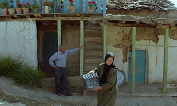 Movie still from “Through the Olive Trees” (1994), directed by Abbas Kiarostami – A man and a woman standing in front of a building; Wide shot, Low angle