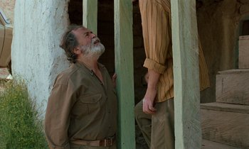 Movie still from “Through the Olive Trees” (1994), directed by Abbas Kiarostami – A man standing next to another man with his mouth open; Medium shot, Low angle