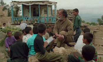 Movie still from “Through the Olive Trees” (1994), directed by Abbas Kiarostami – An older man sitting on a rock with a group of young boys; Medium shot, Over the shoulder angle