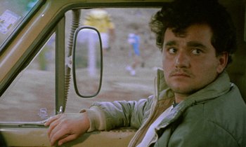 Movie still from “Through the Olive Trees” (1994), directed by Abbas Kiarostami – A man sitting in the driver's seat of a car; Close Up shot, Low angle