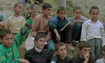 Movie still from “Through the Olive Trees” (1994), directed by Abbas Kiarostami – A group of young men sitting next to each other on the ground; Medium shot, High angle