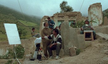 Movie still from “Through the Olive Trees” (1994), directed by Abbas Kiarostami – A group of men sitting on top of a dirt hill; Wide shot, High angle