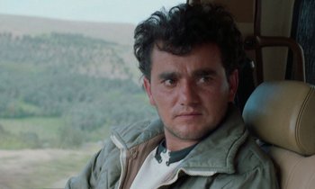 Movie still from “Through the Olive Trees” (1994), directed by Abbas Kiarostami – A person wearing a jacket; Close Up shot, Low angle