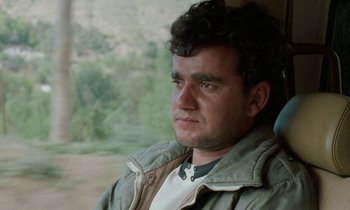 Movie still from “Through the Olive Trees” (1994), directed by Abbas Kiarostami – A person sitting in a car; Close Up shot, Low angle