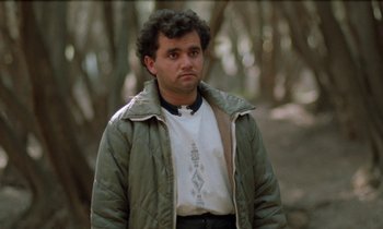 Movie still from “Through the Olive Trees” (1994), directed by Abbas Kiarostami – A man in a white t - shirt and a brown jacket; Medium shot, Low angle