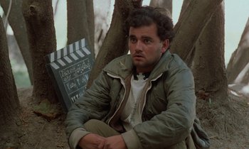 Movie still from “Through the Olive Trees” (1994), directed by Abbas Kiarostami – A man sitting on a tree in the woods; Close Up shot, Low angle