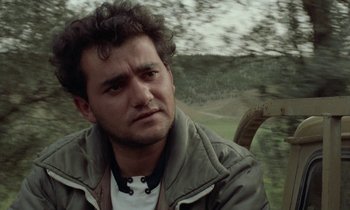 Movie still from “Through the Olive Trees” (1994), directed by Abbas Kiarostami – A person wearing a jacket near a forest; Close Up shot, Low angle