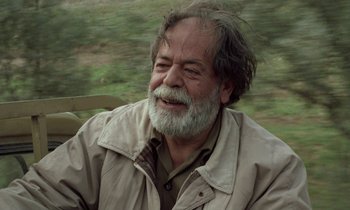 Movie still from “Through the Olive Trees” (1994), directed by Abbas Kiarostami – An older man with a beard and a mustache; Close Up shot, Low angle