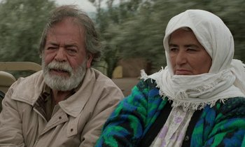 Movie still from “Through the Olive Trees” (1994), directed by Abbas Kiarostami – An older man sitting next to an older woman; Medium shot, High angle
