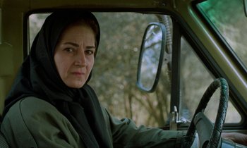Movie still from “Through the Olive Trees” (1994), directed by Abbas Kiarostami – A woman sitting in the driver's seat of a car; Close Up shot, Low angle