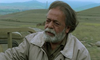 Movie still from “Through the Olive Trees” (1994), directed by Abbas Kiarostami – An older man with a beard and a jacket; Close Up shot, Low angle