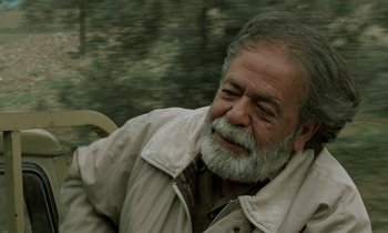 Movie still from “Through the Olive Trees” (1994), directed by Abbas Kiarostami – An older man with a beard and a jacket; Close Up shot, Low angle