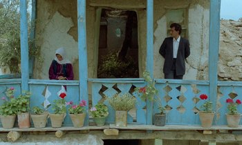 Movie still from “Through the Olive Trees” (1994), directed by Abbas Kiarostami – A man and a woman standing on a balcony; Wide shot, Low angle