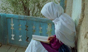 Movie still from “Through the Olive Trees” (1994), directed by Abbas Kiarostami – A woman sitting on the ground reading a book; Medium shot, Low angle