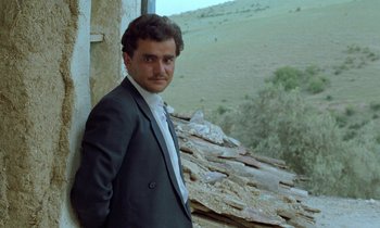 Movie still from “Through the Olive Trees” (1994), directed by Abbas Kiarostami – A man in a suit leaning against a wall; Close Up shot, Low angle