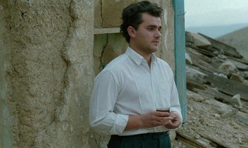 Movie still from “Through the Olive Trees” (1994), directed by Abbas Kiarostami – A man in a white dress shirt is holding a cup; Medium shot, Low angle
