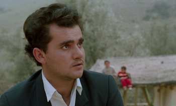 Movie still from “Through the Olive Trees” (1994), directed by Abbas Kiarostami – A man in a black suit looks to his left; Close Up shot, Low angle