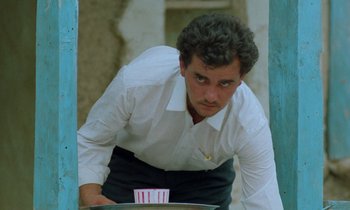 Movie still from “Through the Olive Trees” (1994), directed by Abbas Kiarostami – A man in a white shirt and black skirt looking in a mirror; Close Up shot, Low angle
