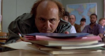 Movie still from “Throw Momma from the Train” (1987), directed by Danny DeVito – A man with a bald head looking at a stack of books; Close Up shot, Low angle