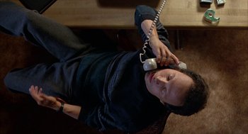 Movie still from “Throw Momma from the Train” (1987), directed by Danny DeVito – A man sitting on the ground talking on a phone; Close Up shot, Overhead angle